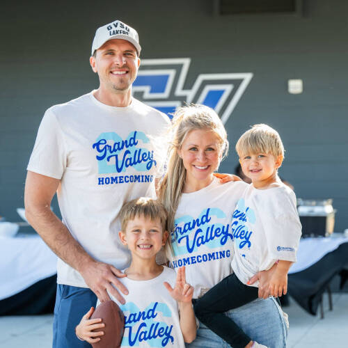Mike Przydzial stands at left with his wife and two sons, all are dressed in Grand Valley homecoming shirts, script GV over a 26